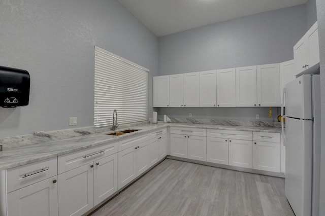 kitchen with white cabinets, sink, light wood-type flooring, white fridge, and light stone counters