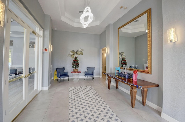 corridor with a chandelier, a raised ceiling, light tile patterned floors, and french doors