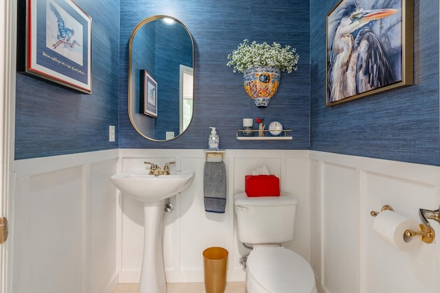 half bathroom featuring a wainscoted wall, wallpapered walls, toilet, and a sink