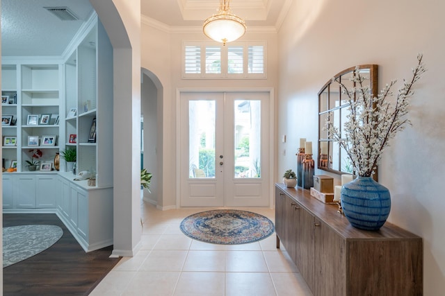 tiled entryway featuring a towering ceiling, crown molding, and french doors