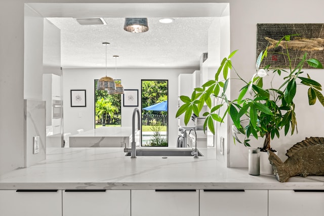 kitchen with light stone counters, white cabinetry, and a textured ceiling