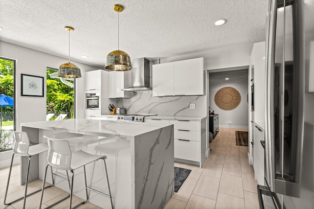 kitchen with decorative light fixtures, white cabinetry, a kitchen island, and wall chimney range hood