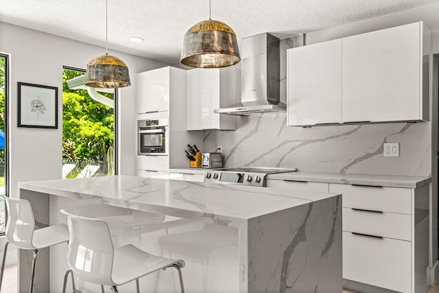 kitchen featuring white cabinetry, hanging light fixtures, and wall chimney range hood