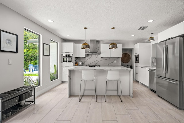 kitchen featuring white cabinetry, wall chimney exhaust hood, pendant lighting, a kitchen island, and appliances with stainless steel finishes