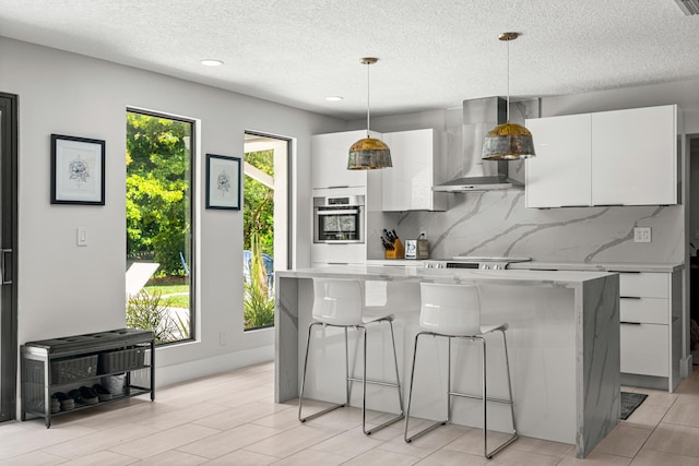 kitchen featuring white cabinetry, wall chimney exhaust hood, hanging light fixtures, backsplash, and oven