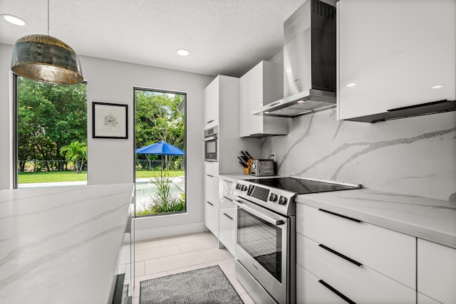 kitchen featuring hanging light fixtures, wall chimney exhaust hood, light stone countertops, white cabinetry, and stainless steel appliances