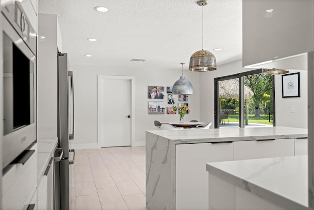 kitchen featuring light stone countertops, a textured ceiling, stainless steel appliances, decorative light fixtures, and white cabinets