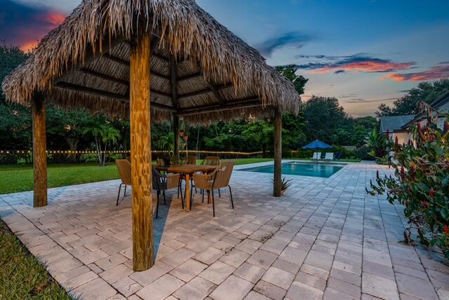 pool at dusk with a gazebo, a patio area, and a lawn