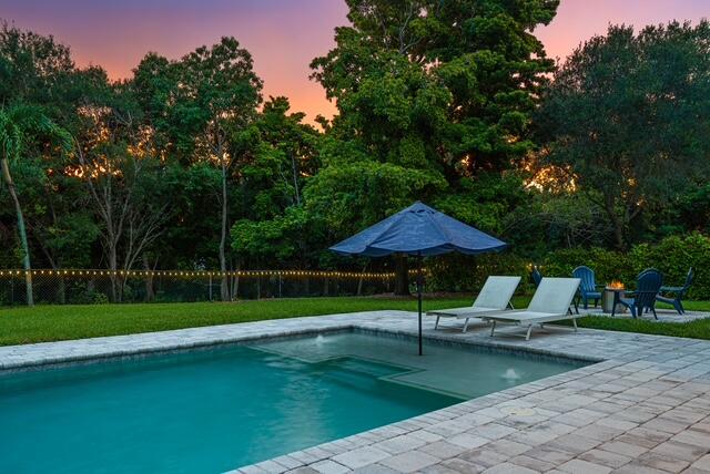 pool at dusk featuring a yard and a patio