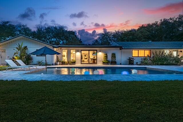 back house at dusk featuring a lawn and a patio