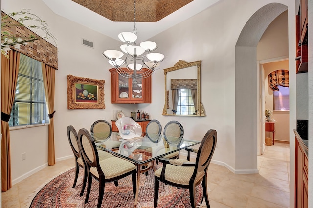 dining room featuring a tray ceiling, light tile patterned flooring, a healthy amount of sunlight, and an inviting chandelier