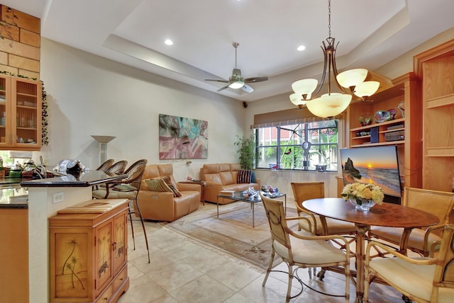 tiled dining room with ceiling fan with notable chandelier and a tray ceiling