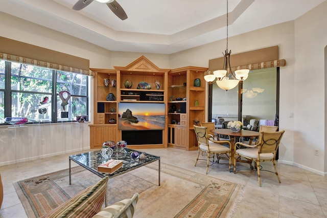 tiled living room featuring a tray ceiling and ceiling fan with notable chandelier