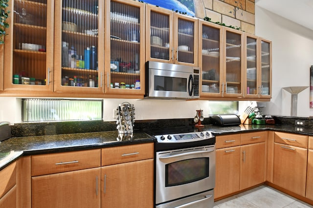 kitchen with dark stone countertops, light tile patterned flooring, and stainless steel appliances