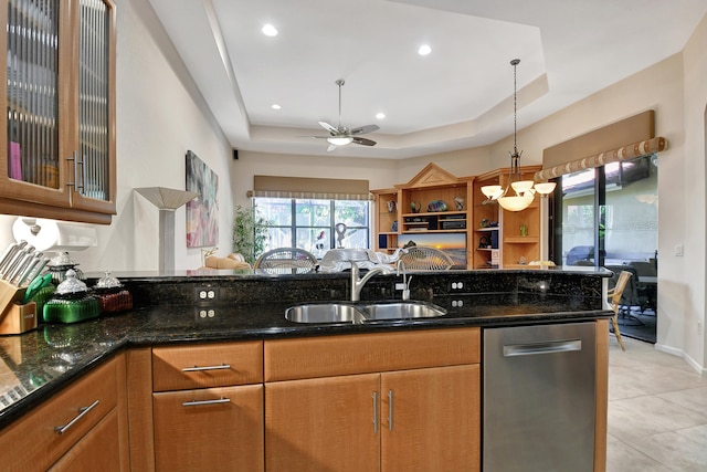 kitchen featuring dark stone counters, a tray ceiling, ceiling fan, sink, and dishwasher