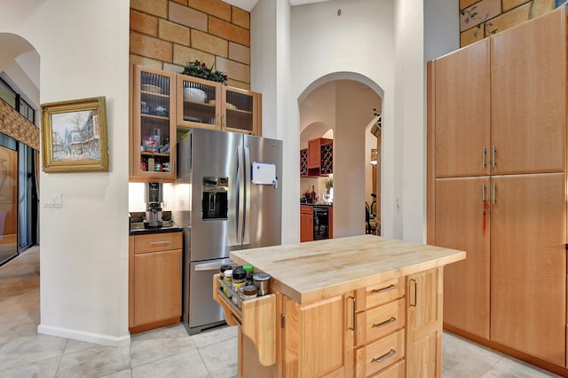 kitchen featuring butcher block counters, a towering ceiling, a kitchen island, stainless steel fridge with ice dispenser, and beverage cooler