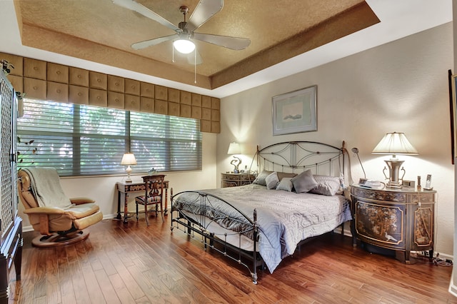 bedroom with a tray ceiling, ceiling fan, hardwood / wood-style floors, and a textured ceiling