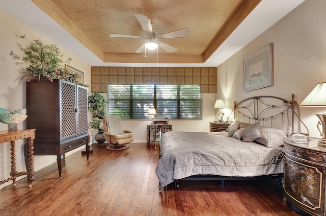 bedroom featuring ceiling fan, wood-type flooring, a textured ceiling, and a tray ceiling