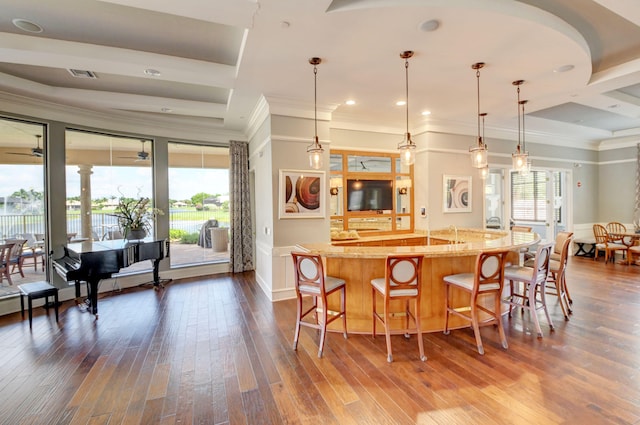 kitchen with hanging light fixtures, hardwood / wood-style flooring, ornamental molding, an island with sink, and a kitchen bar