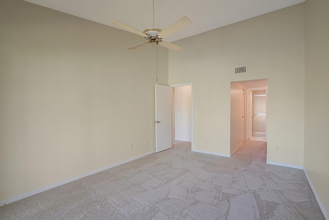 carpeted empty room featuring a towering ceiling and ceiling fan