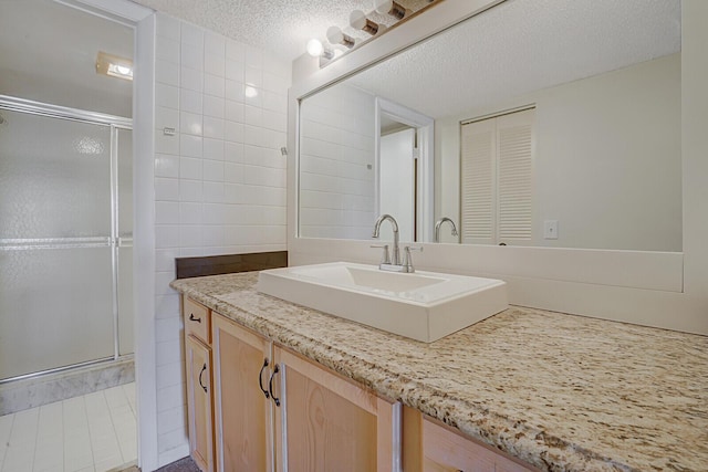 bathroom with walk in shower, vanity, a textured ceiling, and tile walls