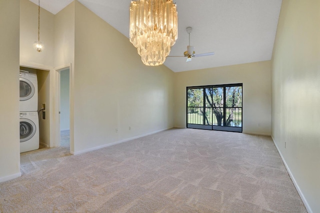 unfurnished room featuring stacked washing maching and dryer, ceiling fan with notable chandelier, light carpet, and high vaulted ceiling