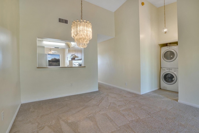 unfurnished dining area with light colored carpet, stacked washing maching and dryer, ceiling fan with notable chandelier, and a high ceiling