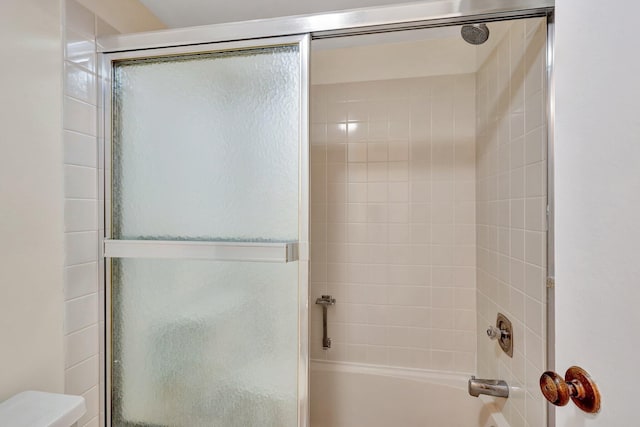 bathroom featuring toilet and shower / bath combination with glass door