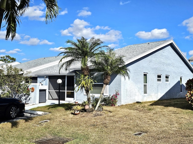 view of front facade featuring stucco siding, a front lawn, roof with shingles, and a sunroom