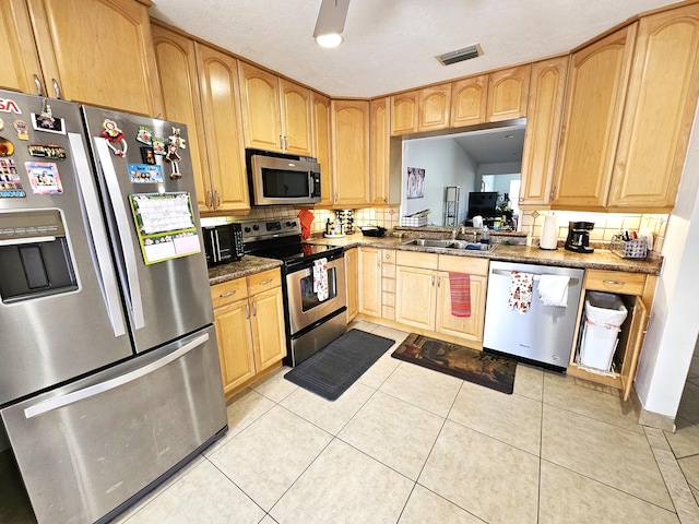 kitchen with tasteful backsplash, stainless steel appliances, sink, dark stone countertops, and light tile patterned flooring