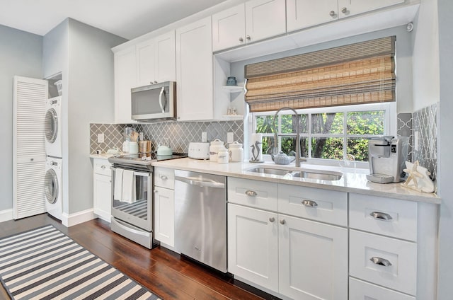 kitchen featuring sink, stainless steel appliances, dark hardwood / wood-style floors, stacked washer and dryer, and white cabinets