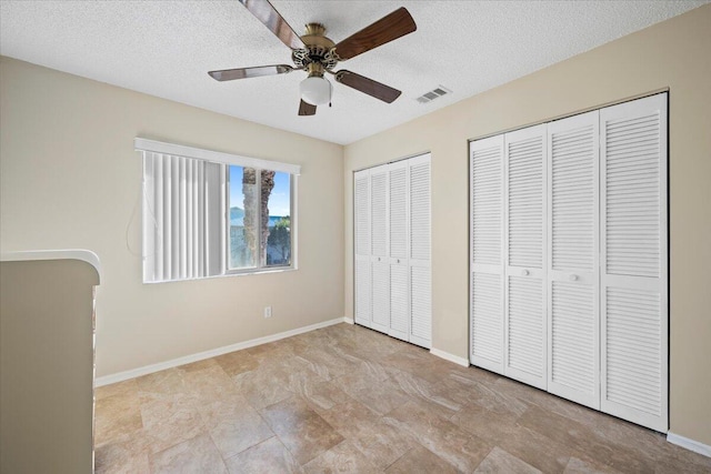 unfurnished bedroom with multiple closets, ceiling fan, and a textured ceiling