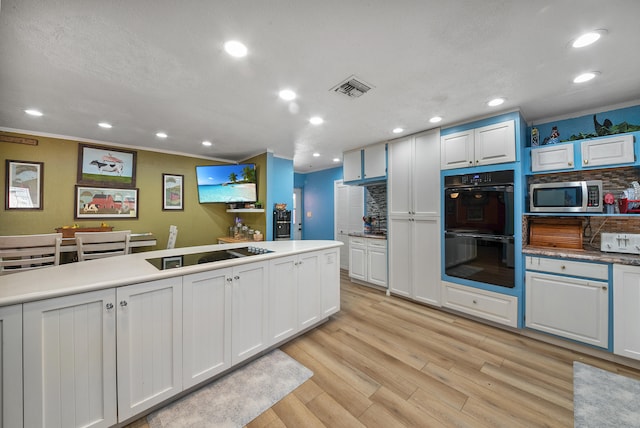 kitchen with white cabinets, black double oven, light hardwood / wood-style flooring, and electric stovetop