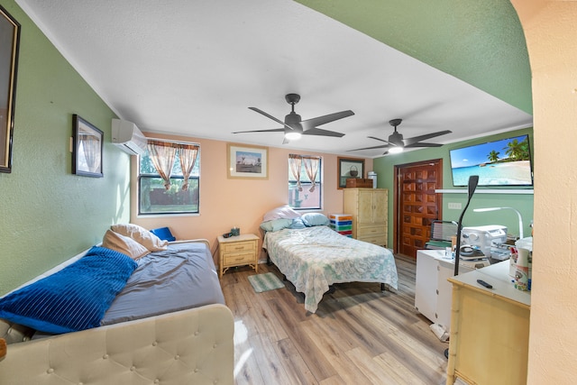 bedroom featuring light hardwood / wood-style flooring, an AC wall unit, multiple windows, and ceiling fan