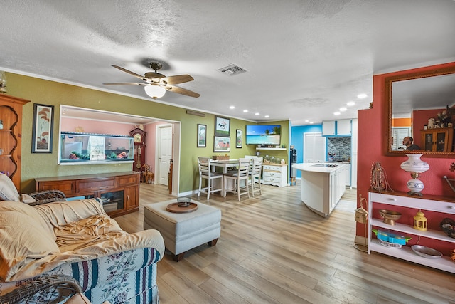 living room with a textured ceiling, light hardwood / wood-style flooring, ceiling fan, and crown molding