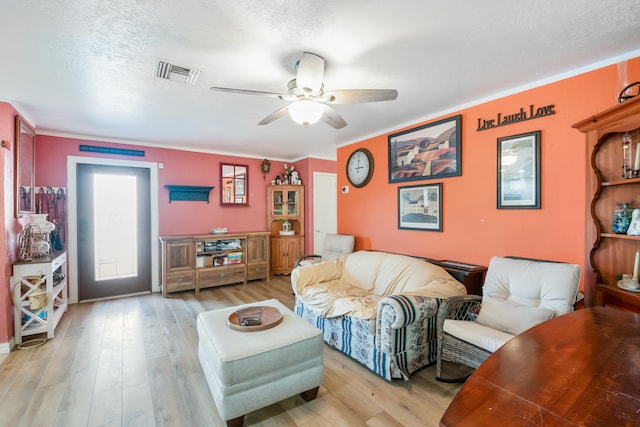 living room with ceiling fan, crown molding, a textured ceiling, and light wood-type flooring