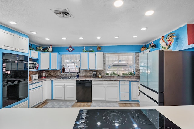 kitchen featuring black appliances, white cabinets, sink, a textured ceiling, and light hardwood / wood-style floors