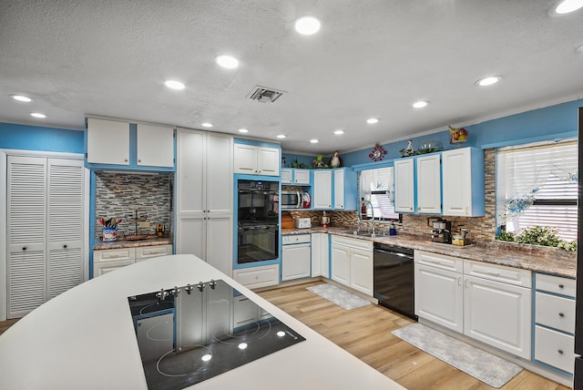 kitchen with white cabinetry, sink, black appliances, and light hardwood / wood-style flooring