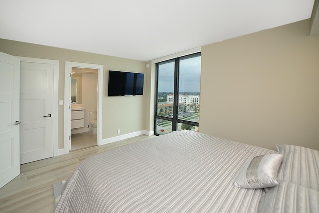 bedroom with ensuite bathroom, light hardwood / wood-style flooring, and expansive windows