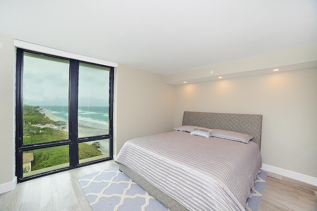 bedroom with a water view, light hardwood / wood-style flooring, and multiple windows