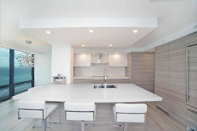 kitchen featuring kitchen peninsula, hanging light fixtures, a breakfast bar, a water view, and wall chimney exhaust hood