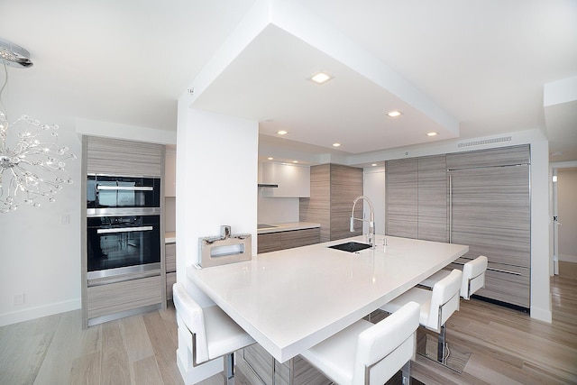 kitchen with an island with sink, a kitchen bar, sink, and light hardwood / wood-style flooring