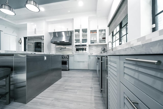 kitchen featuring tasteful backsplash, wall chimney range hood, a breakfast bar, white cabinetry, and high end appliances