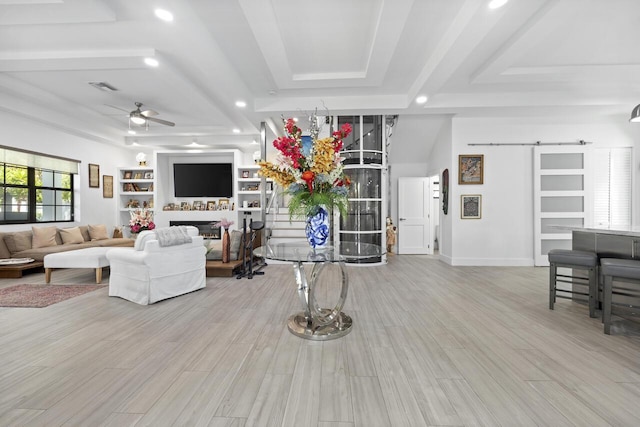 living area featuring a barn door, visible vents, a raised ceiling, a ceiling fan, and a fireplace