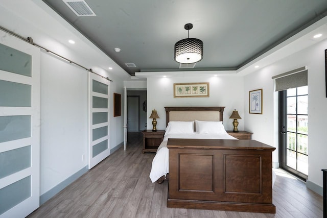 bedroom featuring recessed lighting, visible vents, a barn door, and wood finished floors