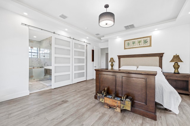 bedroom featuring a barn door, ensuite bathroom, and light hardwood / wood-style floors