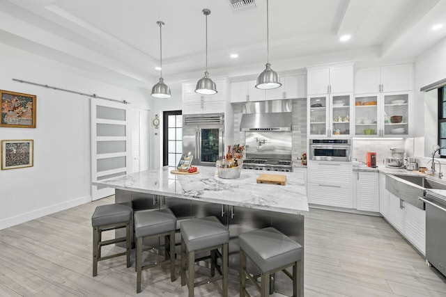 kitchen featuring a barn door, appliances with stainless steel finishes, a kitchen island, white cabinetry, and extractor fan