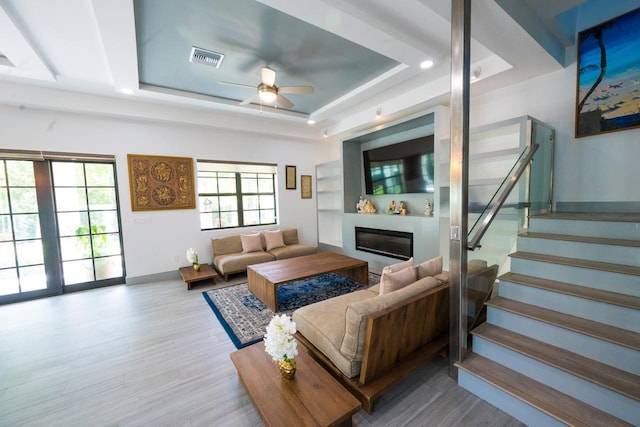 living area featuring a glass covered fireplace, a tray ceiling, a ceiling fan, and visible vents