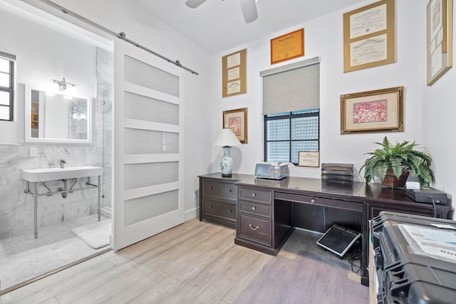 office space with a barn door, ceiling fan, built in features, and light wood-type flooring