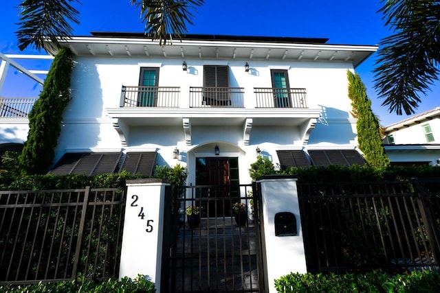 view of front of property with stucco siding, a balcony, a fenced front yard, and a gate